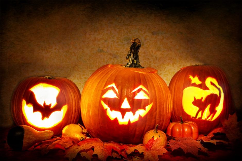 Glowing Halloween jack-o’-lanterns surrounded by autumn leaves