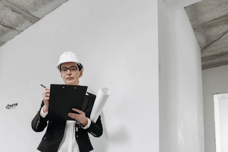 Illustrative stock photo of an engineer in a hard hat reviewing building plans.